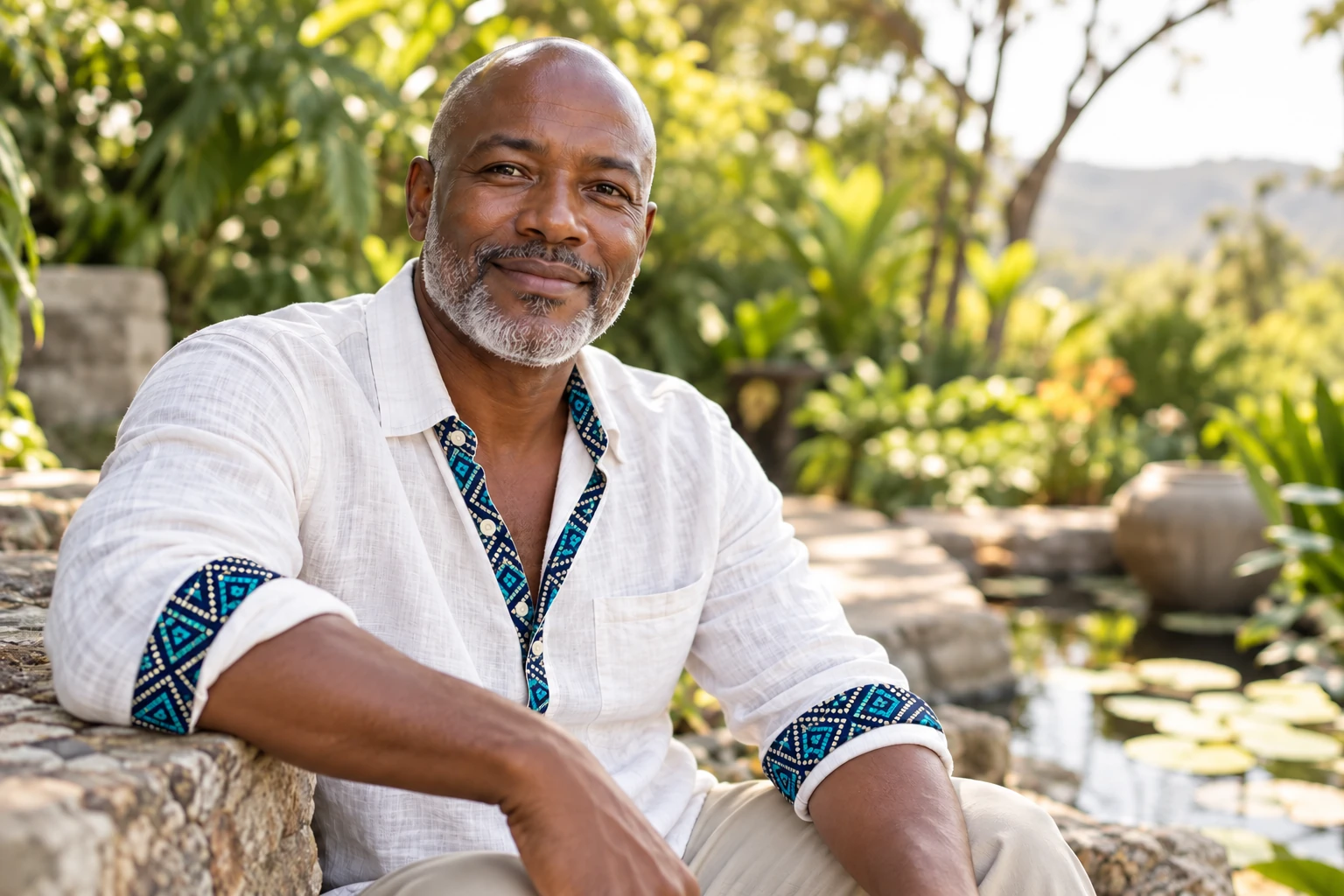 Un homme souriant porte une chemise blanche avec des détails Ankara bleu marine et turquoise dans un jardin